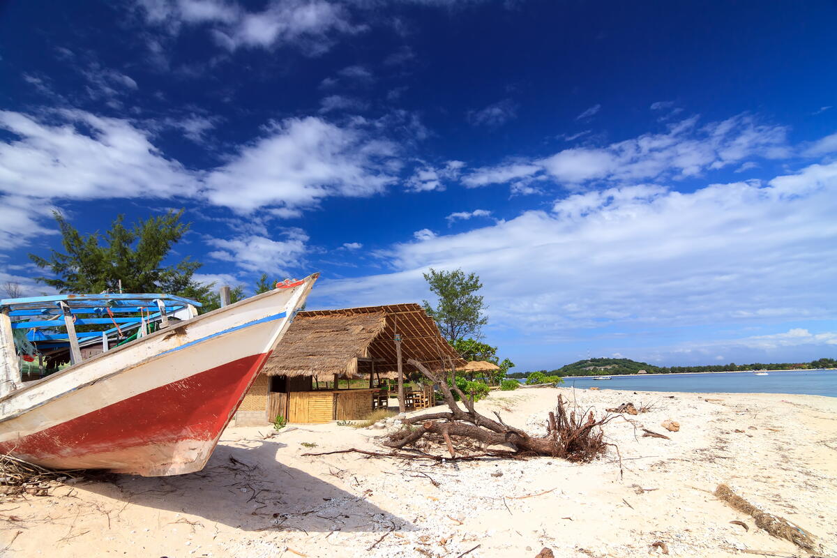 Ein ehemaliges Fischerboot liegt am Strand von Lombok neben einer Hütte unter einem strahlend blauen Himmel.