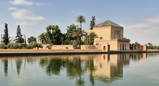 Ein Pavillon spiegelt sich im klaren Wasser des Ménaragartens in Marrakesch unter einem sonnigen Himmel.