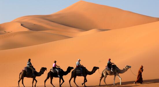 Eine Gruppe von Menschen reitet auf Kamelen durch die beeindruckenden Dünen der Sahara.