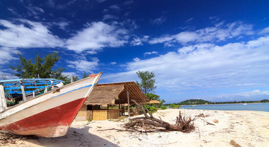 Ein ehemaliges Fischerboot liegt am Strand von Lombok neben einer Hütte unter einem strahlend blauen Himmel.