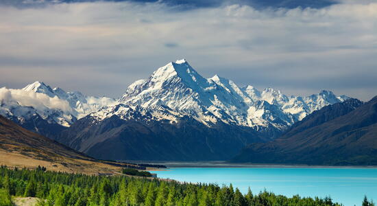 Der Blick auf den schneebedeckten Mount Cook zeigt majestätisch den türkisfarbenen See und die umgebenden Wälder.